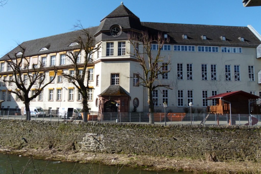 Beispielhaft für die Betreuenden Grundschulen in Dillenburg ist hier das Gebäude der Juliane-von-Stolberg-Schule dargestellt. Ein großes, weißes Gebäude mit einem fast turmartigen Eingangsbereich von dem jeweils zwei Gebäudeflügel links und rechts abweichen.