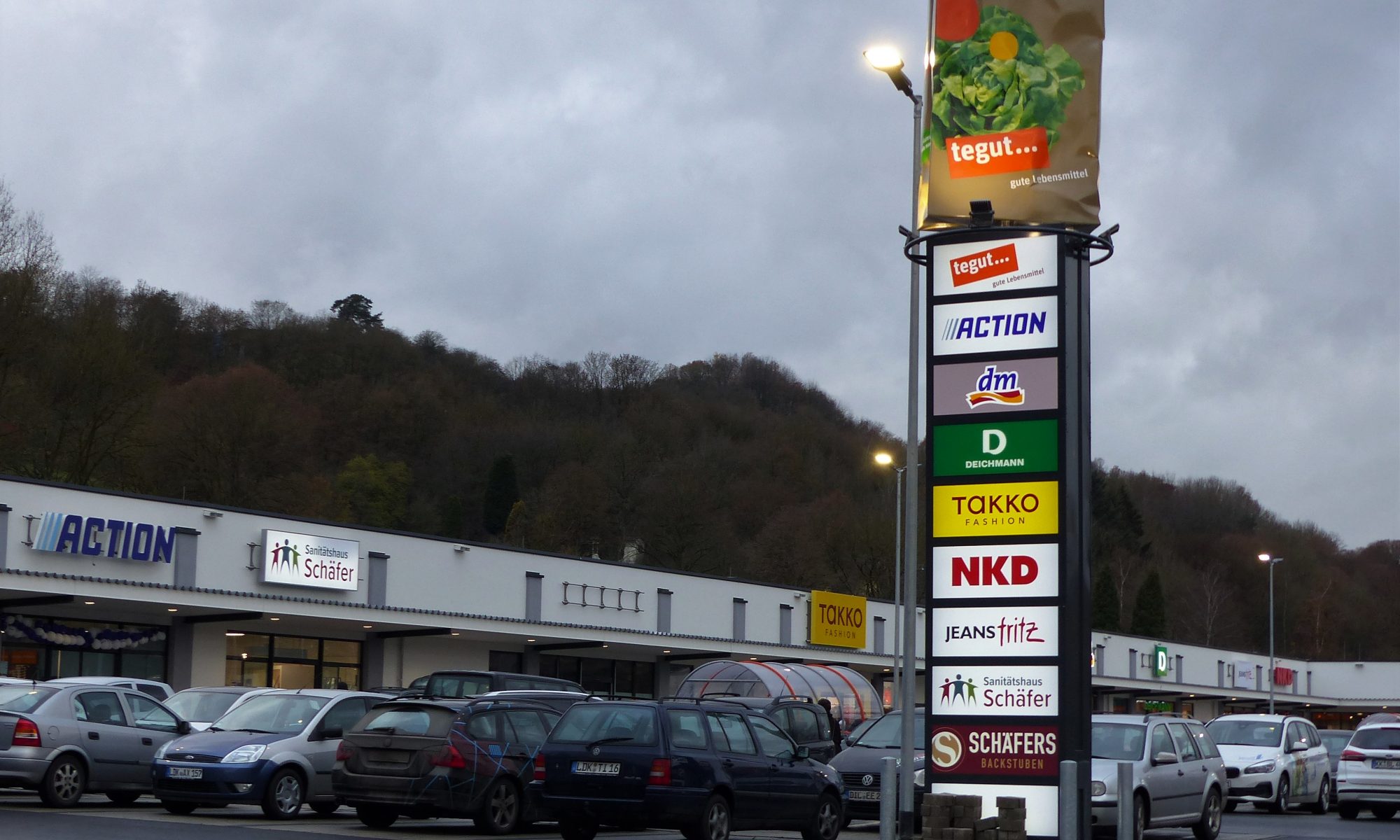 Ein Bild vom Parkplatz des Fachmarktzentrums mit einigen der Geschäften und der Werbestehle