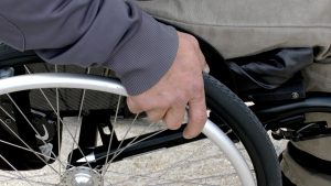 Ein Bildausschnitt mit einer Hand am Rad eines Rollstuhls