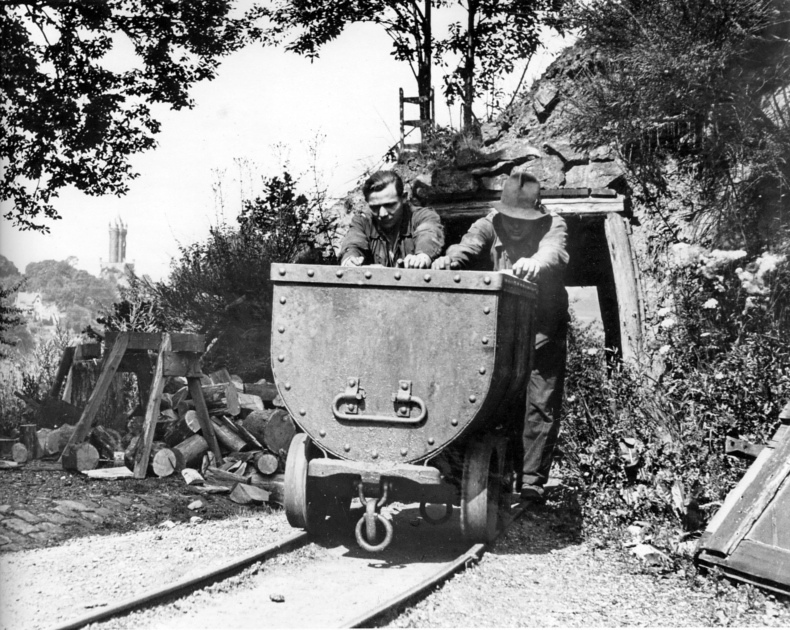 Eine Schwarz-Weiß-Fotografie der Grube „Laufenderstein“ in Dillenburg um 1940. Zwei Bergarbeiter schieben eine Lohre. Im Hintergrund der Wilhelmsturm (Foto: Sammlung Rolf Georg)