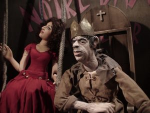 Das Bild zeigt zwei der Marionetten, die bei den Dillenburger Figuren Theater Tagen gespielt werden. Links eine weibliche Puppe mit dunklen lockigen Haaren und einem roten Ballkleid, rechts eine Marionette, die wie ein König mit Krone gekleidet ist und auf einem Thron sitzt.