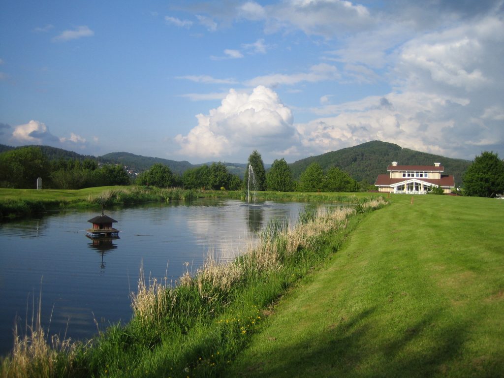 Eine Ansicht des Golplatzes mit Teich im Vordergrund und Clubhaus im Hintergrund.