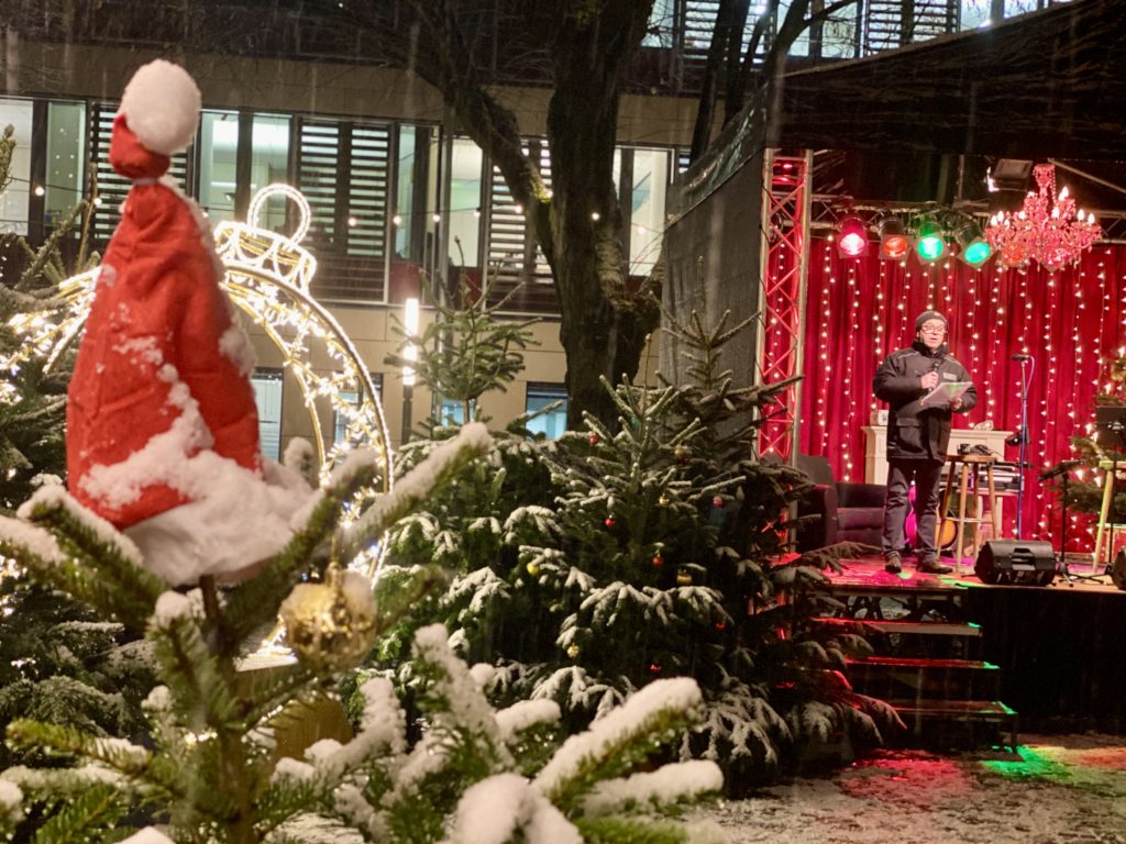 Am linken Bildrand ist ein Teil eines Christbaums mit einer Nikolausmütze zu sehen. Am rechten Bildrand sieht man die Bühne.