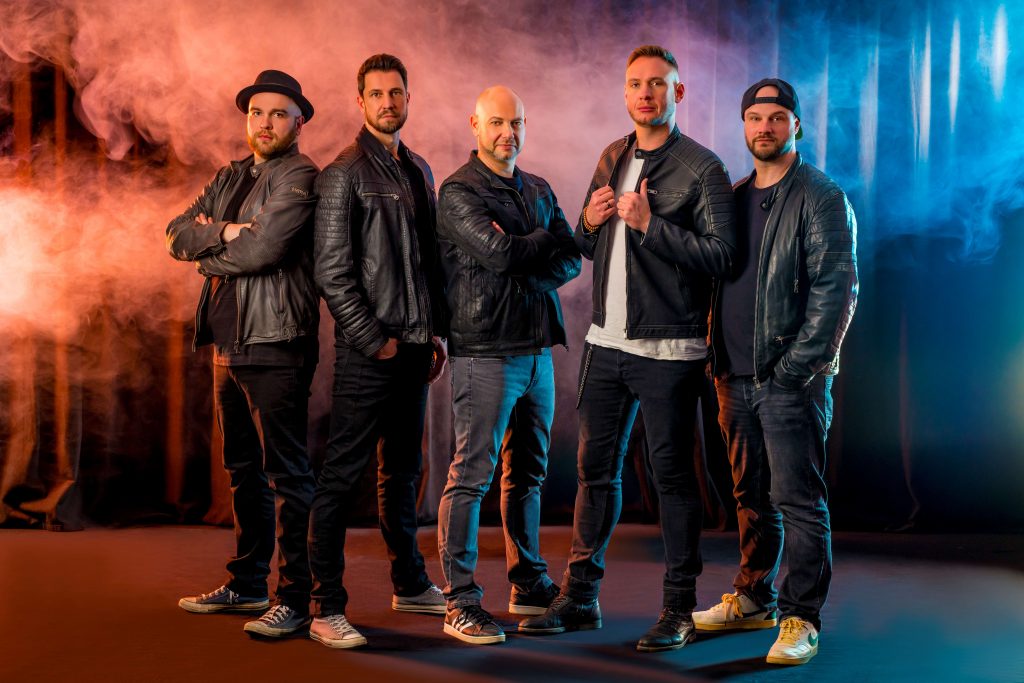 Bandfoto der Gruppe Still Counting. Fünf Männer in Lederjacken auf einer beleuchteten Bühne