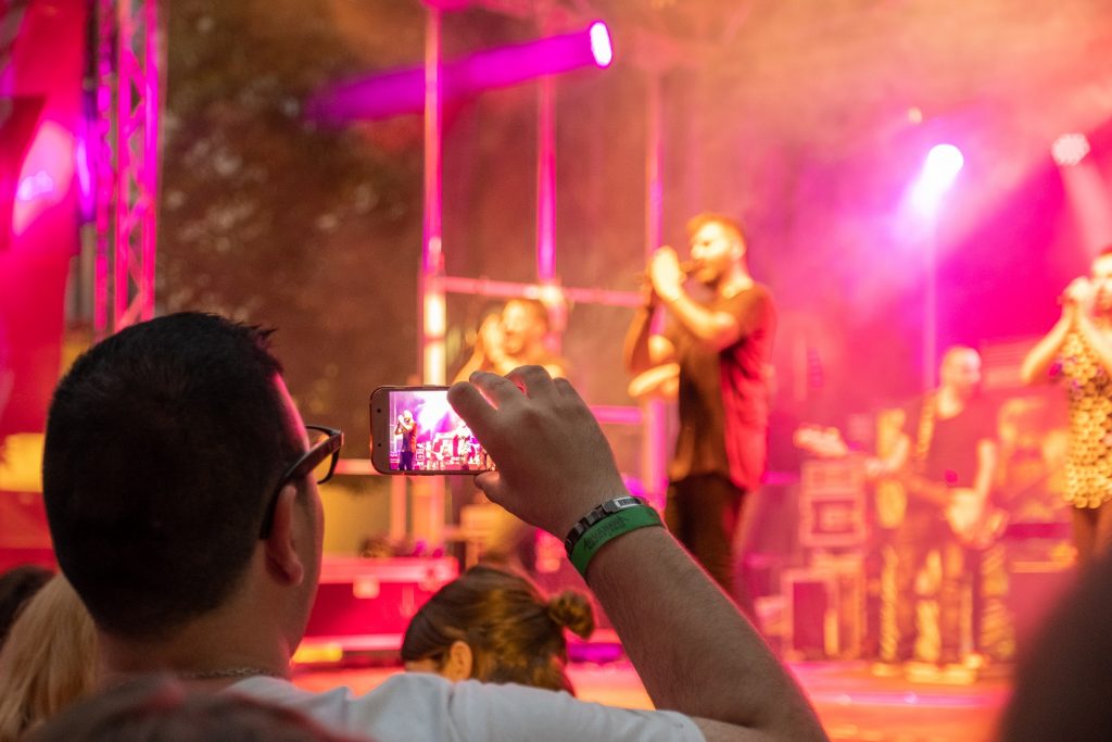 Ein Konzertbesucher filmt durch sein Handy die Band auf der Bühne