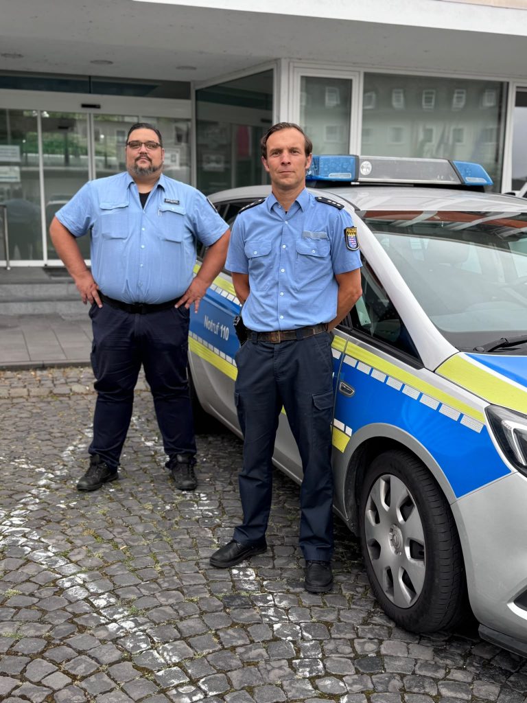 Der Schutzmann Marcus Hippenstiel und Ordnungspolizeibeamter Eike Estevez Kring an einem Polizeiauto vor dem Stadthaus Herefordhaus.
