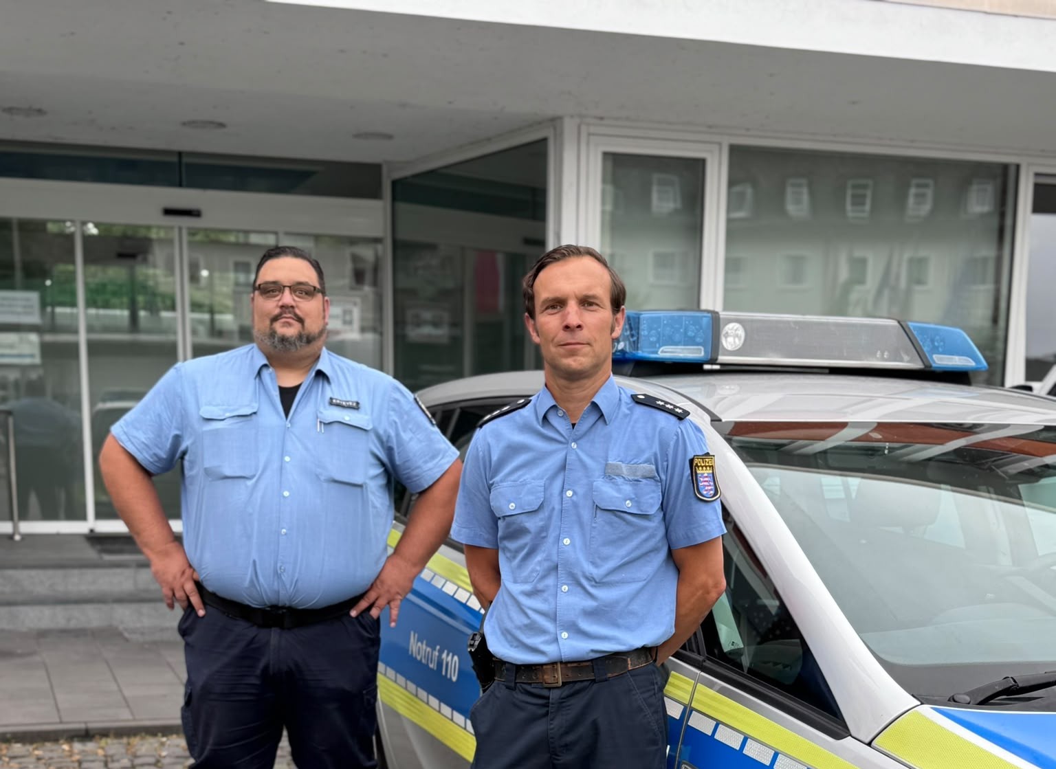 PHK Marcus Hippenstiel und Ordnungspolizeibeamter der Oranienstadt Dillenburg Eike Estevez Kring an einem Polizeiauto vor dem Stadthaus Herefordhaus. Mit Klick aufs Bild geht´s zum Artikel