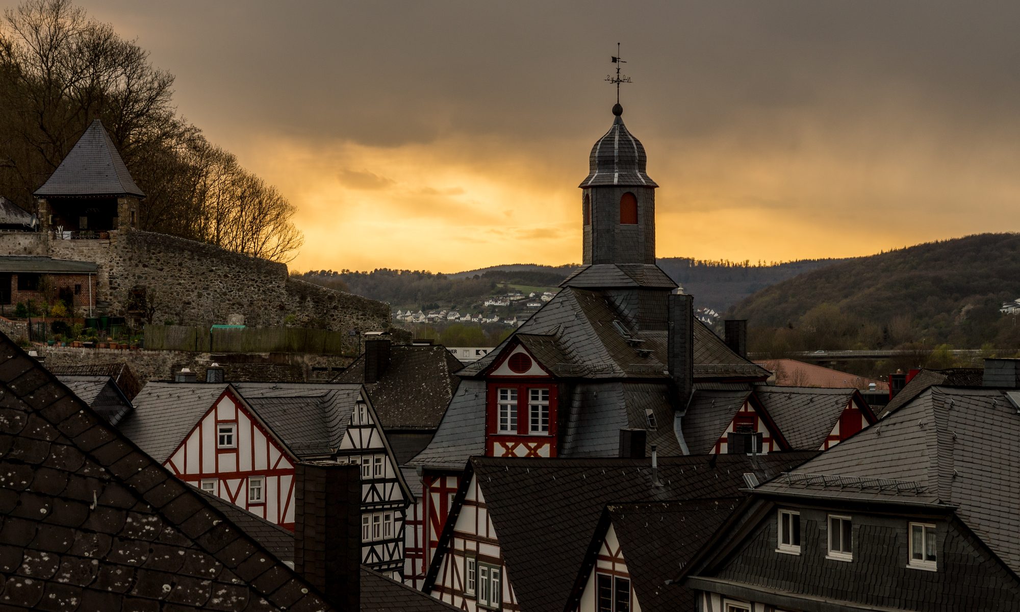 Das Alte Rathaus in Dillenburg und die umgebenden Fachwerkhäuser vor einem Abendhimmel, an dem graue Wolken aufziehen.