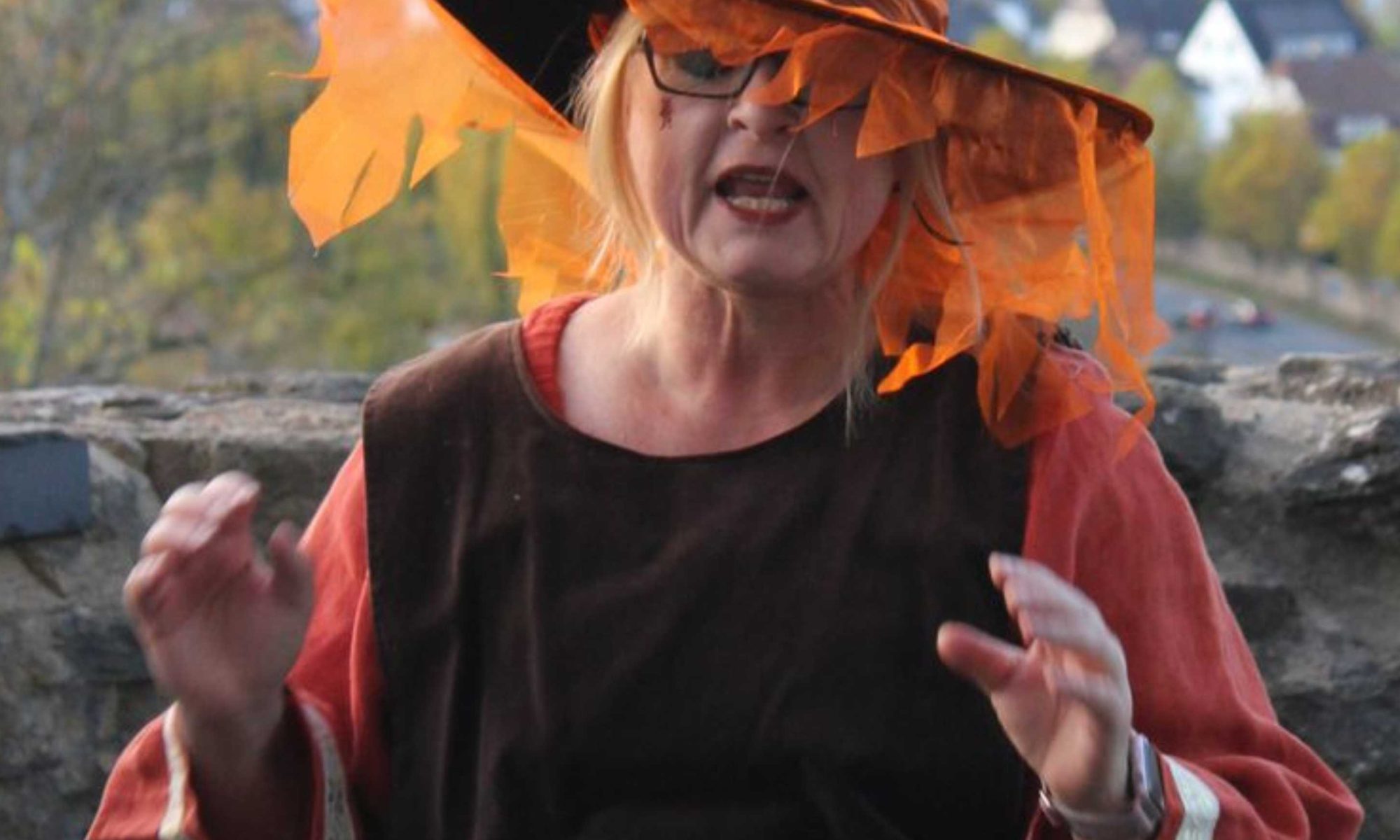 Eine als Hexe verkleidete Frau in braun und orange gehaltenem Kostüm und mit spitzem Hut.