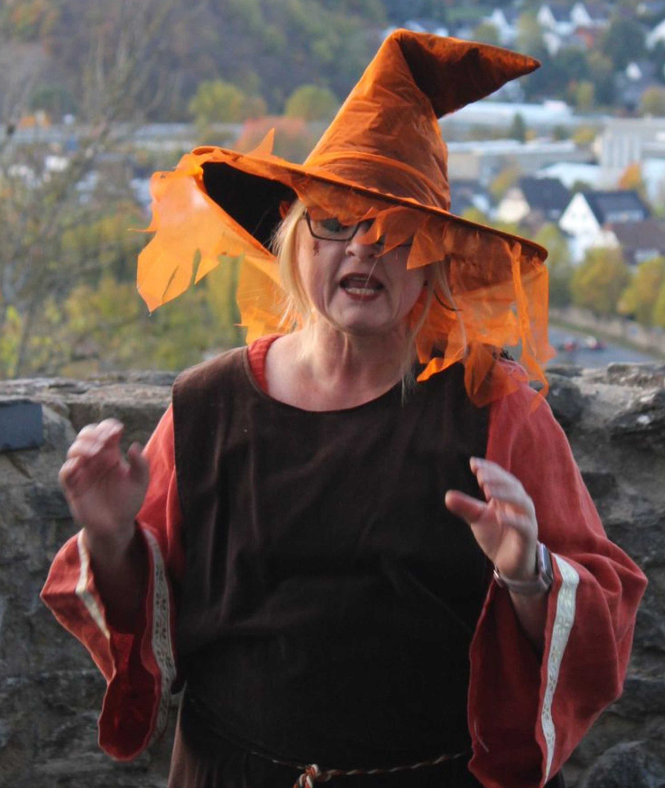 Eine als Hexe verkleidete Frau in braun und orange gehaltenem Kostüm und mit spitzem Hut.